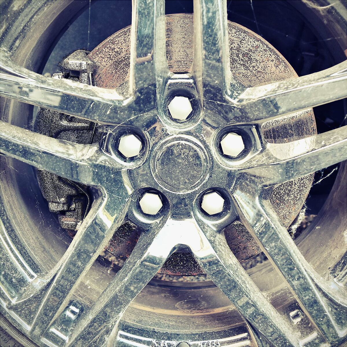 Dirty silver five-spoke alloy with dust, cobwebs and a dull finish